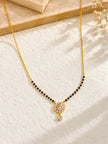 CZ mangalsutra with black beads and gold chain laid flat on a textured white surface with dried flowers