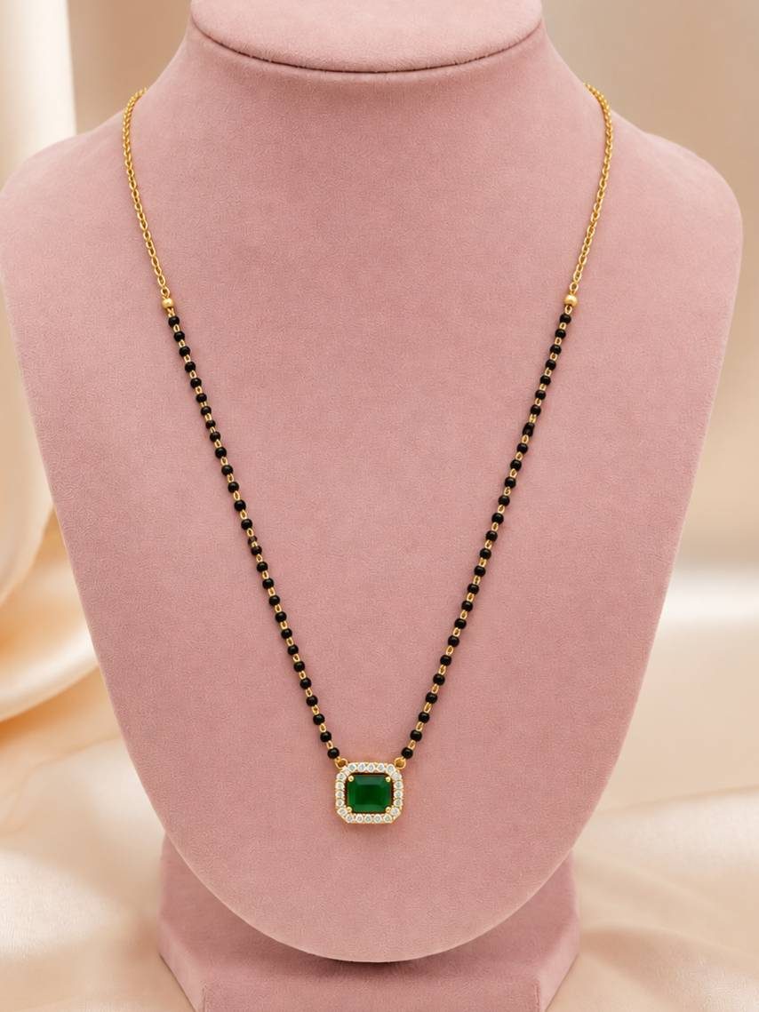 Gold-plated mangalsutra with emerald green CZ pendant displayed on a pink jewellery bust