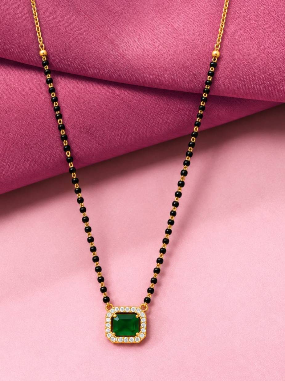 Black bead gold-tone mangalsutra with square green stone pendant on pink fabric background