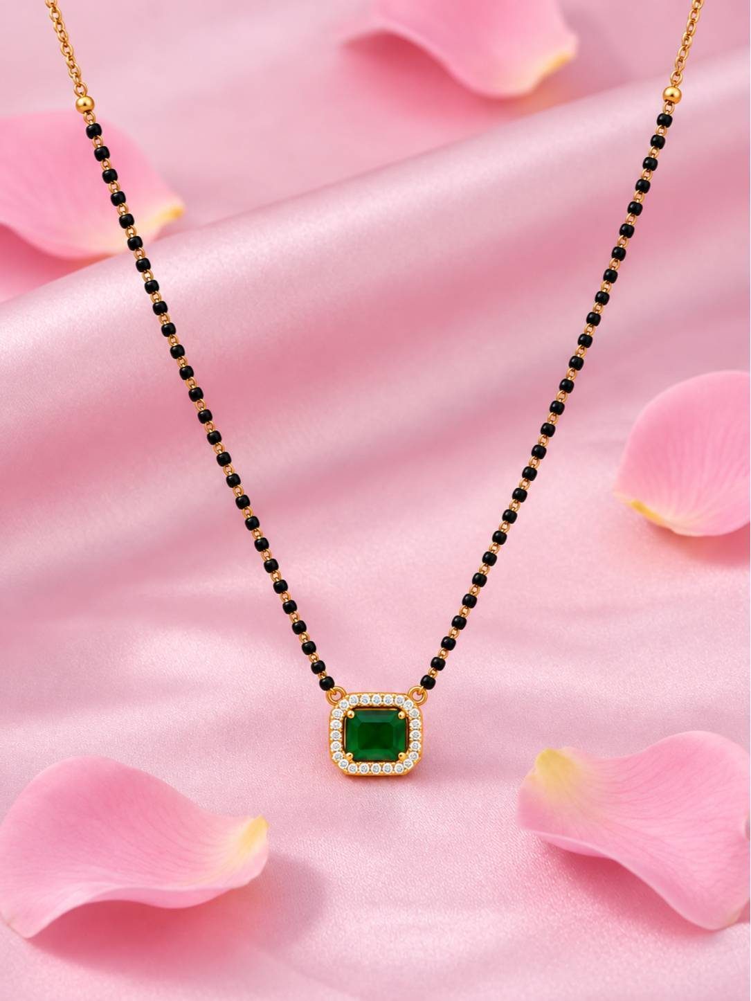 Emerald green CZ mangalsutra laid flat on pink satin surrounded by rose petals