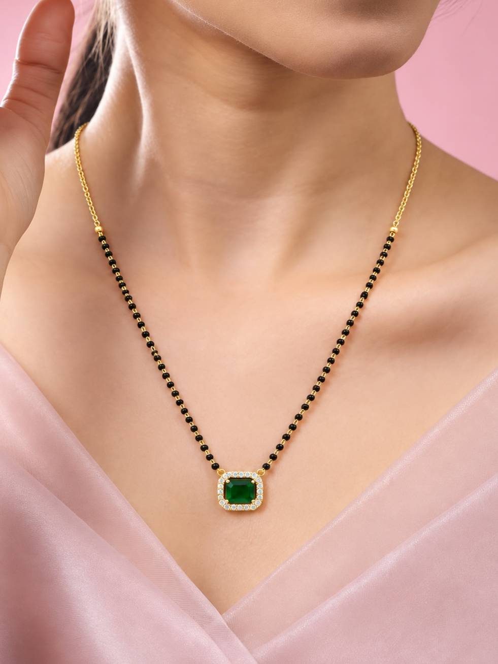 Woman wearing gold-plated emerald green CZ mangalsutra against a soft pink top