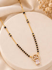 Gold-plated black bead mangalsutra with CZ circular pendant and baguette stone drop laid on a round cream surface