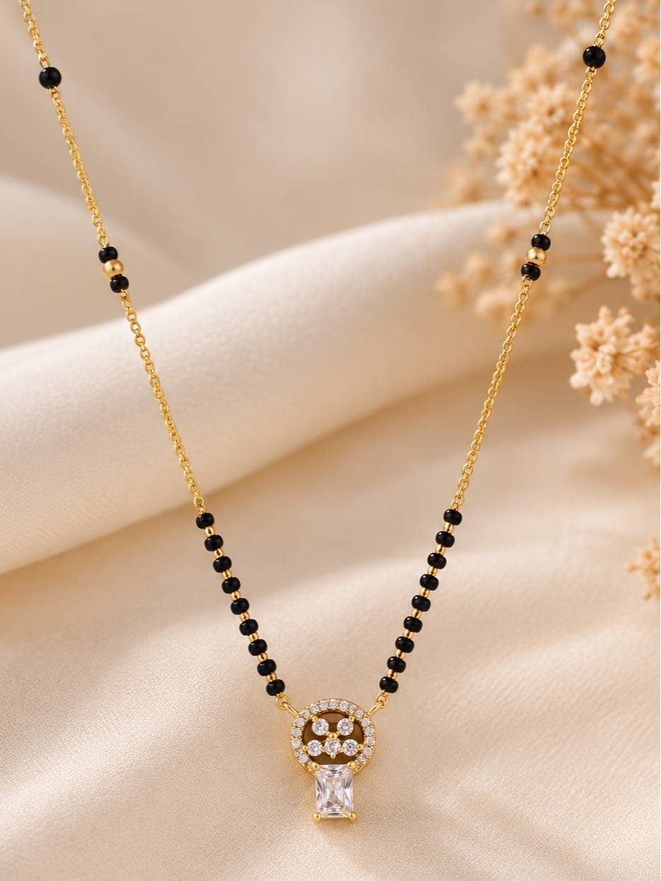 Close-up of gold mangalsutra with black beads and diamond-studded round pendant on cream fabric with dried flowers