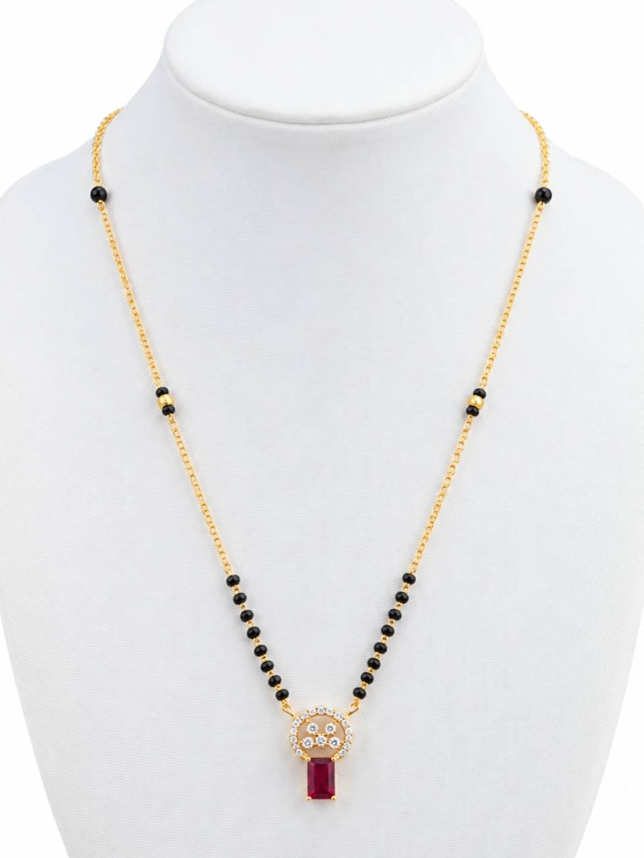 Gold-plated black bead mangalsutra with circular CZ and ruby-red pendant displayed on white jewellery bust