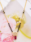 Close-up of mangalsutra pendant showing CZ stones and deep red rectangular gemstone laid flat near pink roses