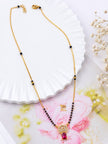 Full-length gold-plated black bead mangalsutra with lobster clasp laid on white decorative dish with dried florals