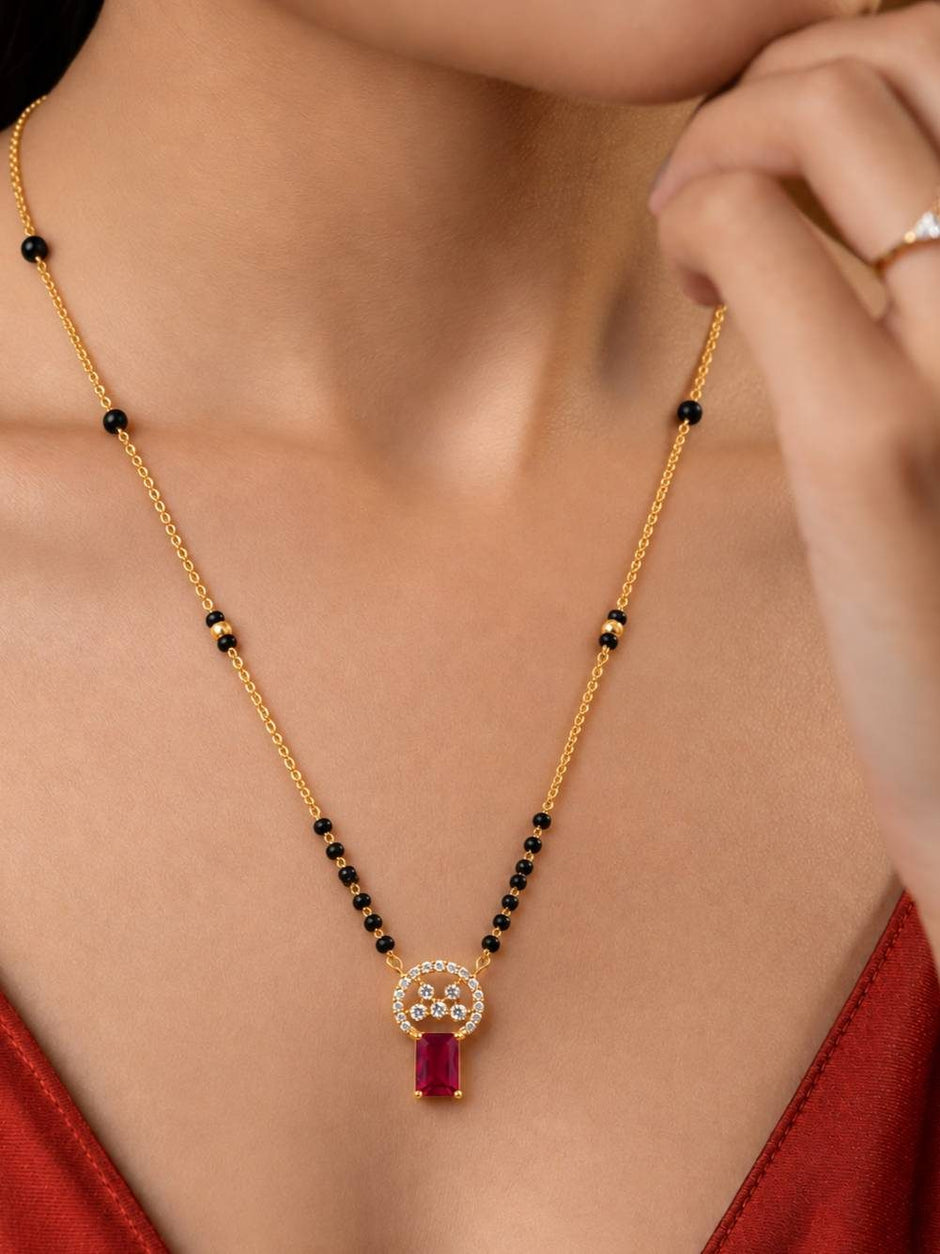 Woman wearing gold-plated black bead mangalsutra with ruby CZ pendant over red outfit, neck close-up