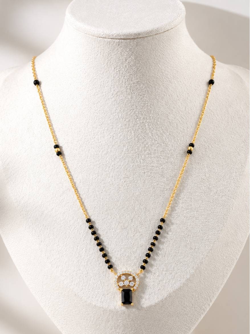 Gold-plated black bead mangalsutra with CZ circular pendant and black emerald-cut drop displayed on white jewellery bust