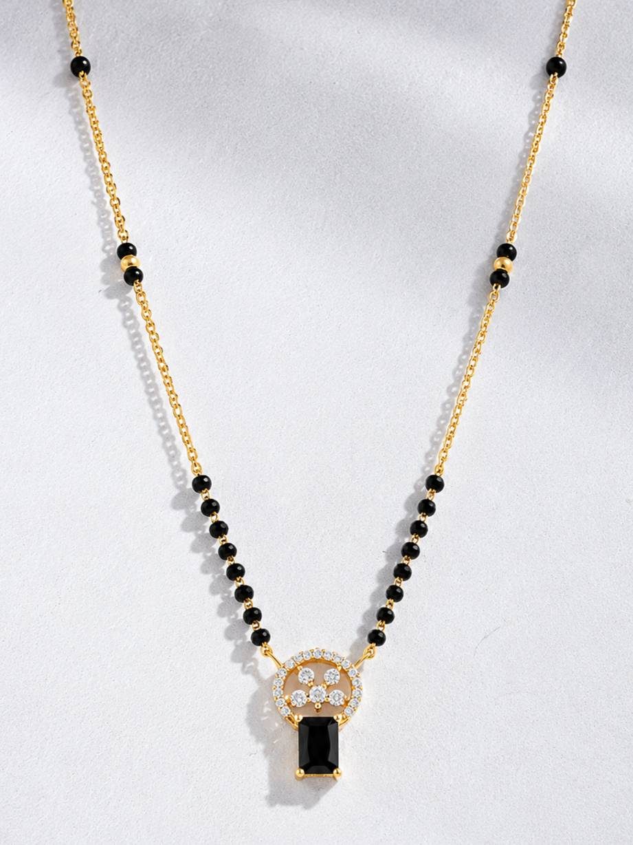 Close-up of gold-plated black bead mangalsutra with CZ circular pendant on grey background