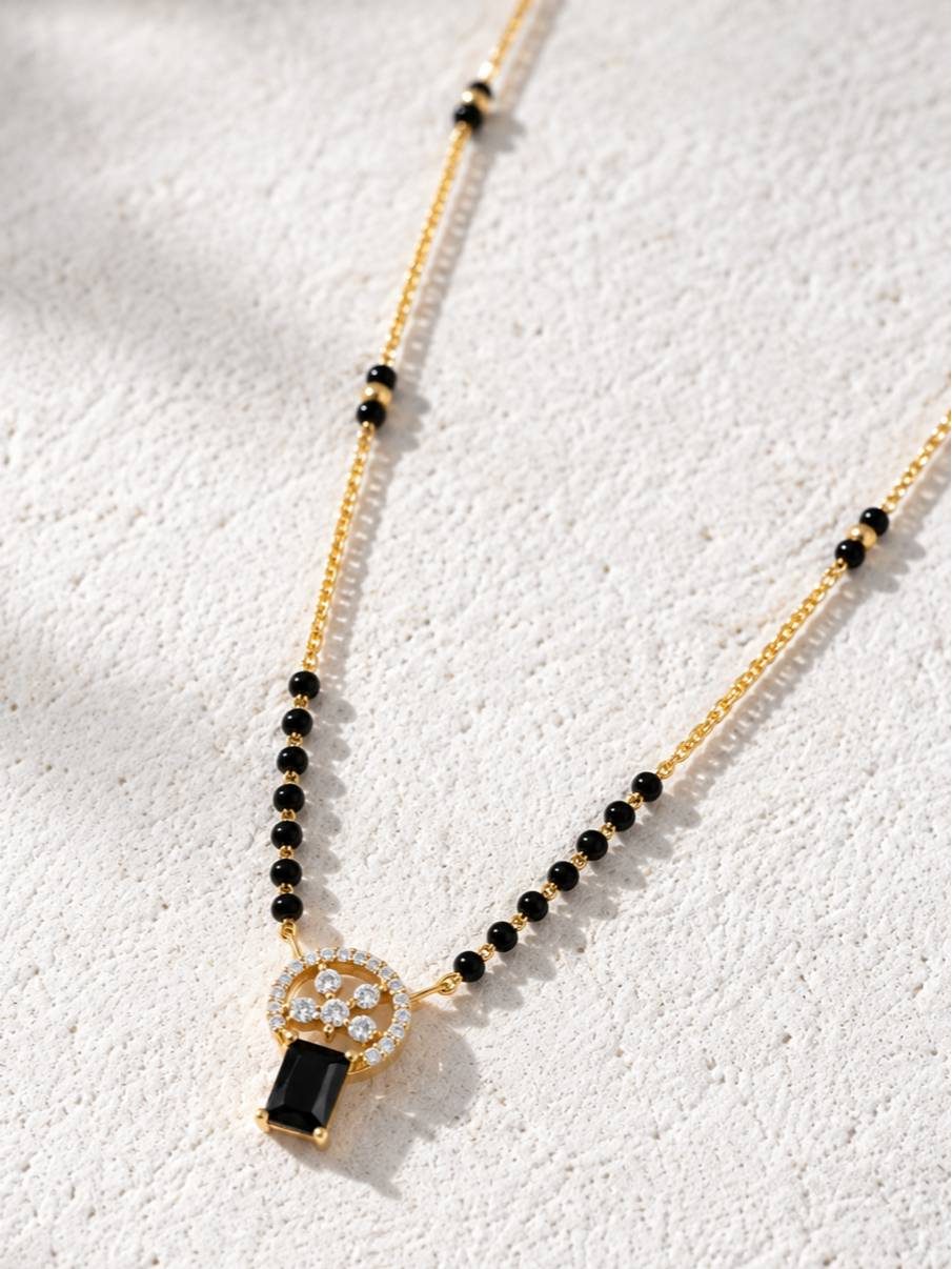 Full length view of gold-plated black bead mangalsutra with CZ pendant laid flat on textured white surface