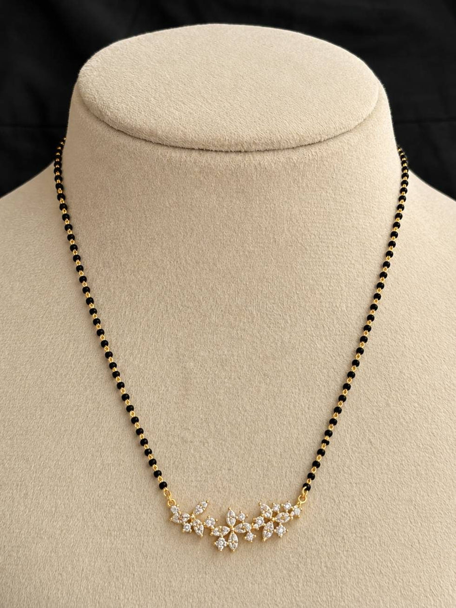 Gold-plated CZ floral mangalsutra with black beads displayed on a beige jewellery bust