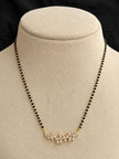 Gold-plated CZ floral mangalsutra with black beads displayed on a beige jewellery bust