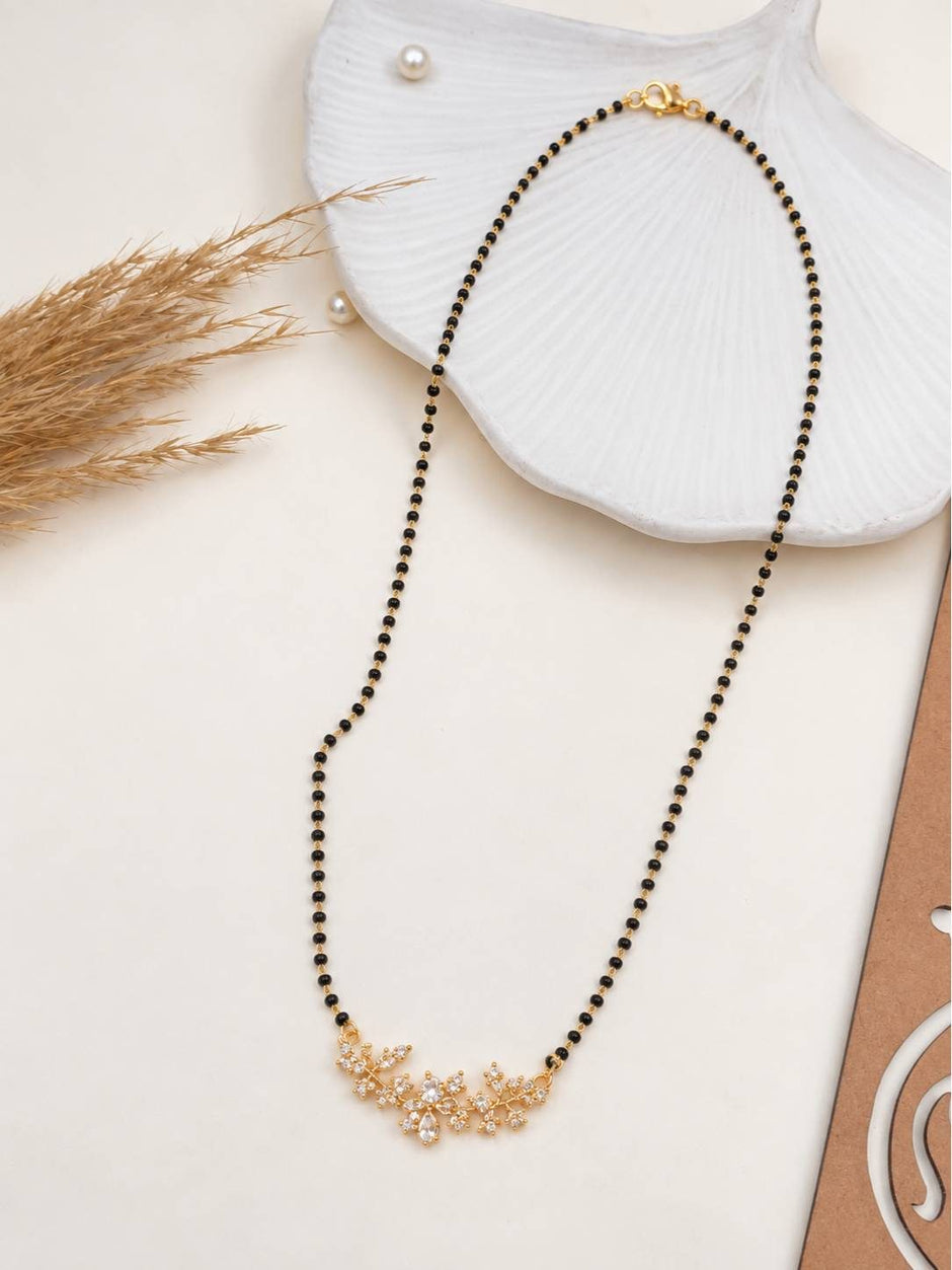 CZ floral mangalsutra laid flat on white surface beside a decorative shell and dried grass