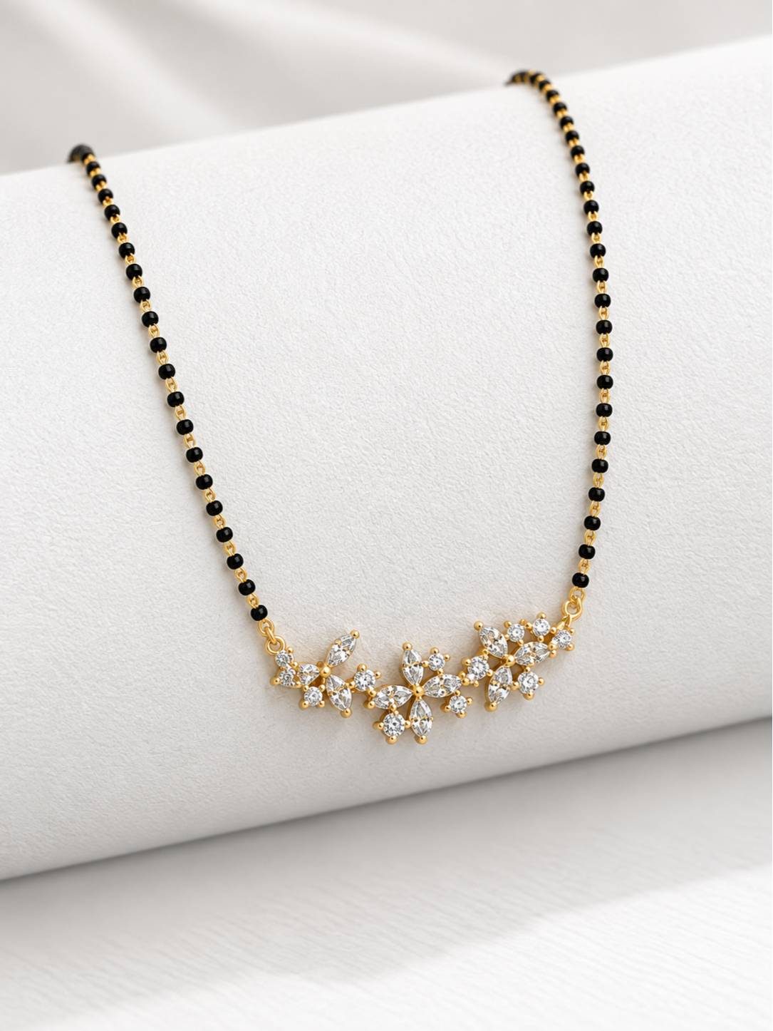 Close-up of three CZ flower pendant motifs on gold-plated mangalsutra draped over a white roll