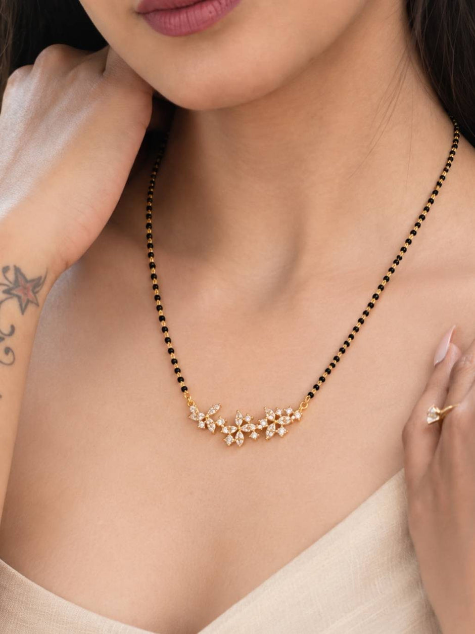 Woman wearing gold-plated CZ floral mangalsutra with black-bead chain over a beige outfit