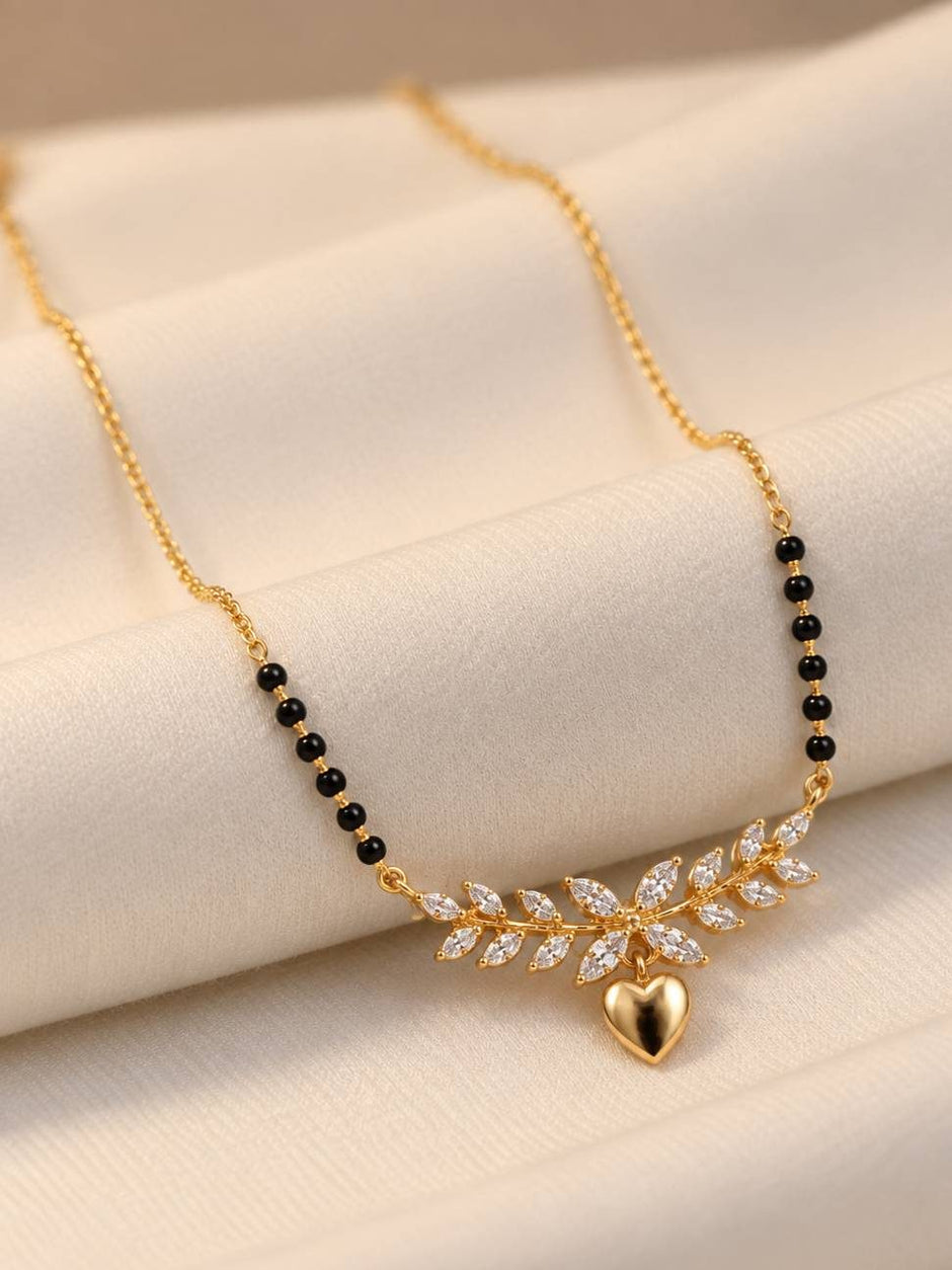 Close-up of gold-plated mangalsutra with black beads and cubic zirconia leaf motif laid on white fabric