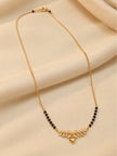 Full-length view of gold-plated black bead mangalsutra with leaf and heart pendant on cream fabric
