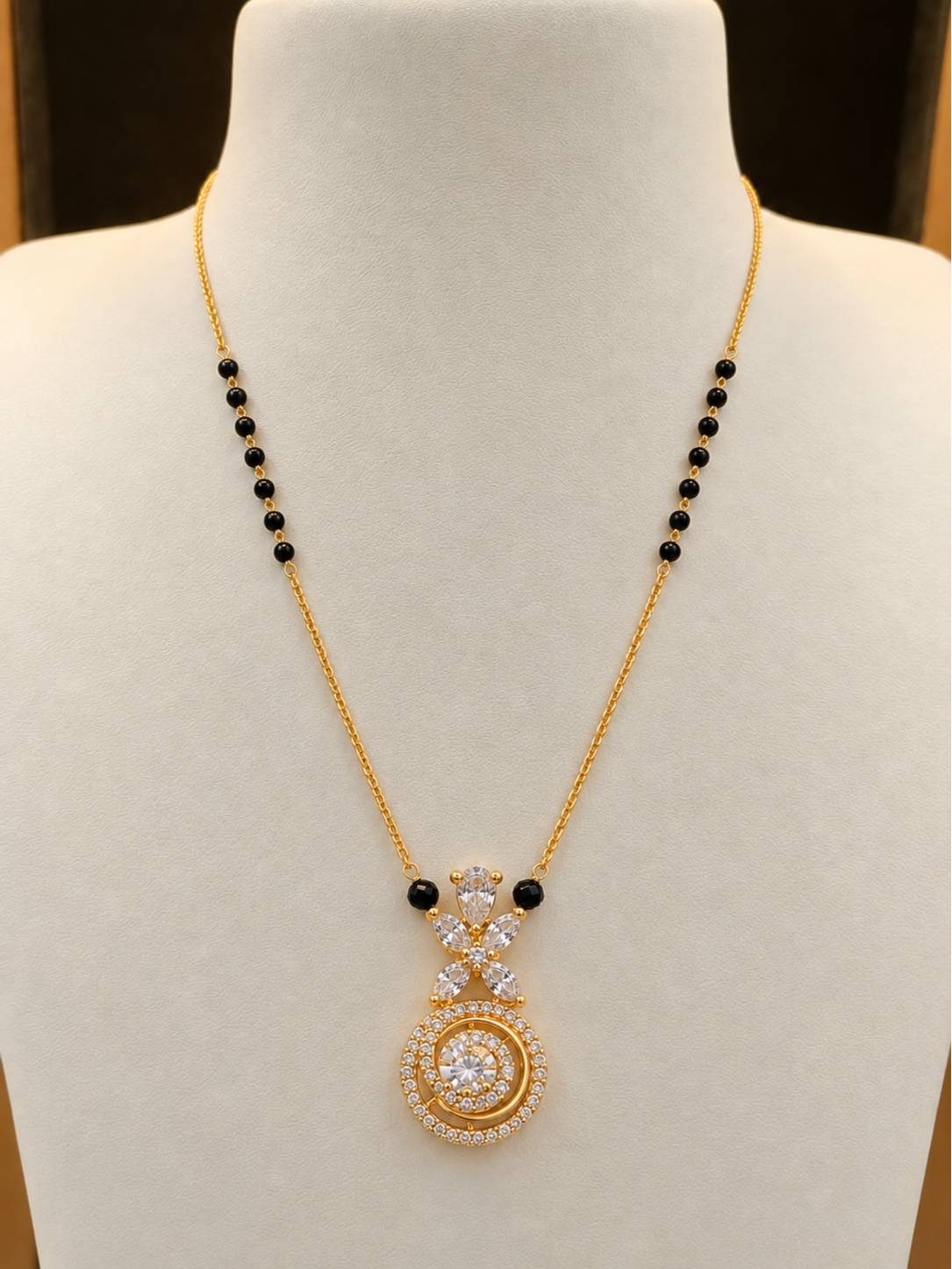 Gold-plated CZ mangalsutra with black beads displayed on a white jewellery bust