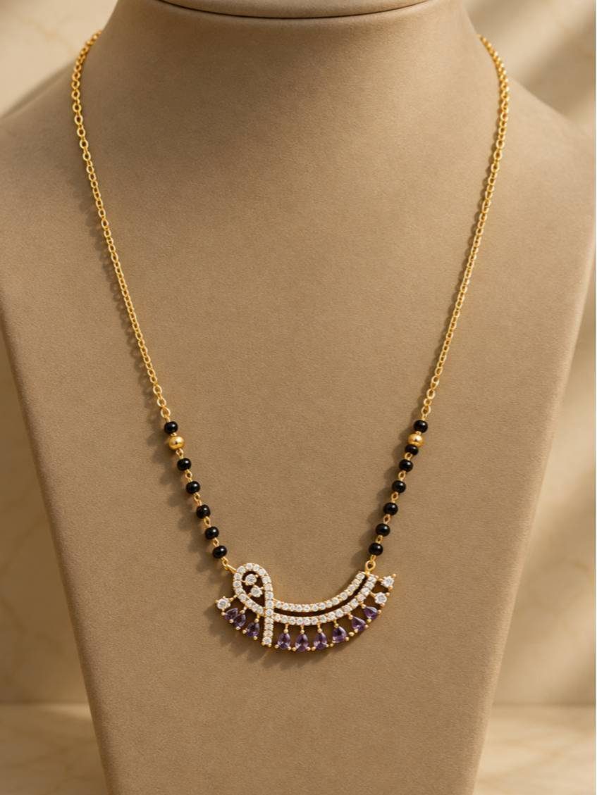 Gold-plated mangalsutra with black beads and purple CZ fan pendant displayed on a beige jewellery bust