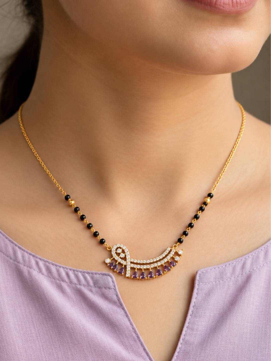 Model wearing gold-plated black bead mangalsutra with purple stone pendant over a lavender kurta