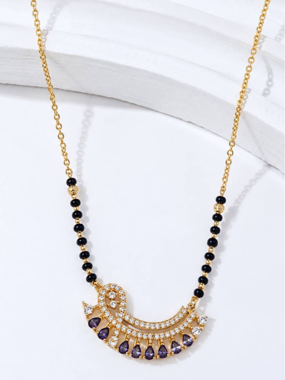 Close-up of crescent mangalsutra pendant showing white cubic zirconia and purple teardrop stones on white background