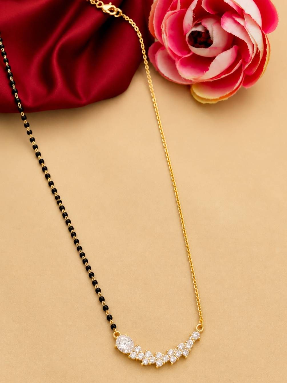 Mangalsutra with CZ bar pendant laid flat beside a pink rose on peach background