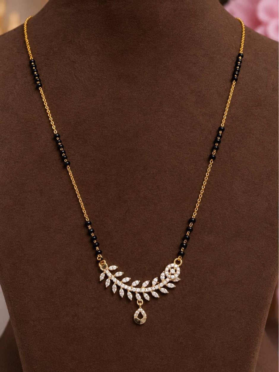 Gold-plated CZ leaf mangalsutra displayed on a brown jewellery bust showing black bead chain and teardrop drop