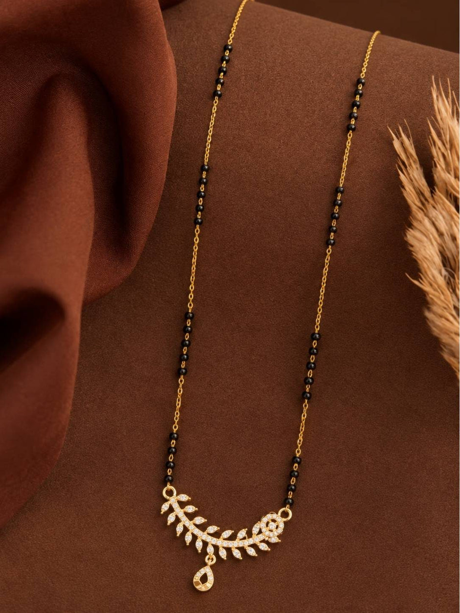 Full-length view of gold-plated CZ mangalsutra laid flat on a brown draped fabric with dried grass styling prop