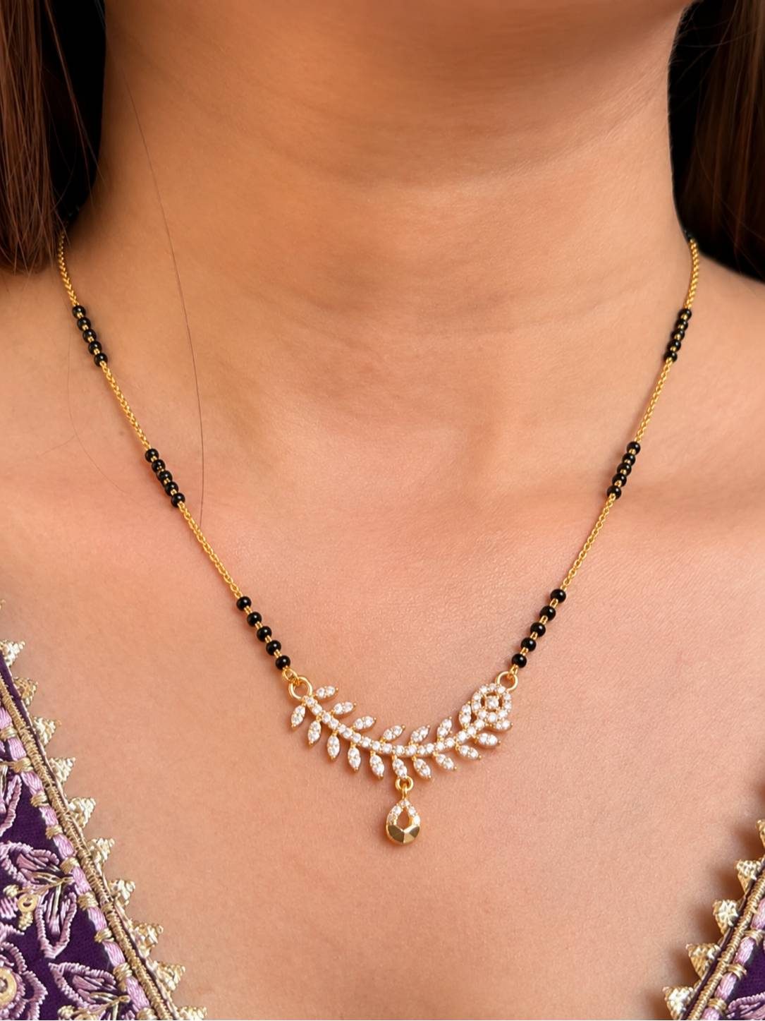 Gold-plated CZ mangalsutra worn around a woman's neck over a purple embroidered ethnic outfit