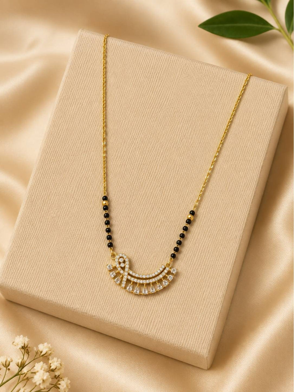 Gold-plated CZ mangalsutra with fan pendant displayed on a cream jewellery box with flowers