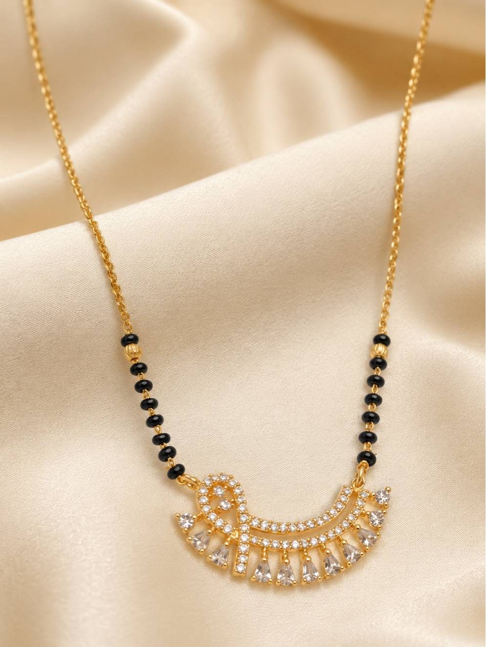 Close-up of gold-plated mangalsutra showing black beads and cubic zirconia fan pendant on satin