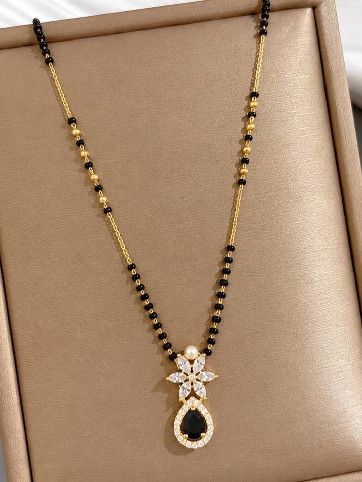Gold-plated black bead mangalsutra with CZ floral pendant displayed on a beige jewellery tray