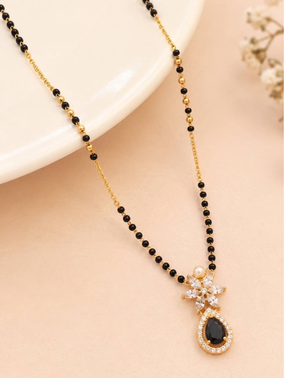 Black bead mangalsutra with white CZ marquise and black teardrop pendant on a cream stand with flowers
