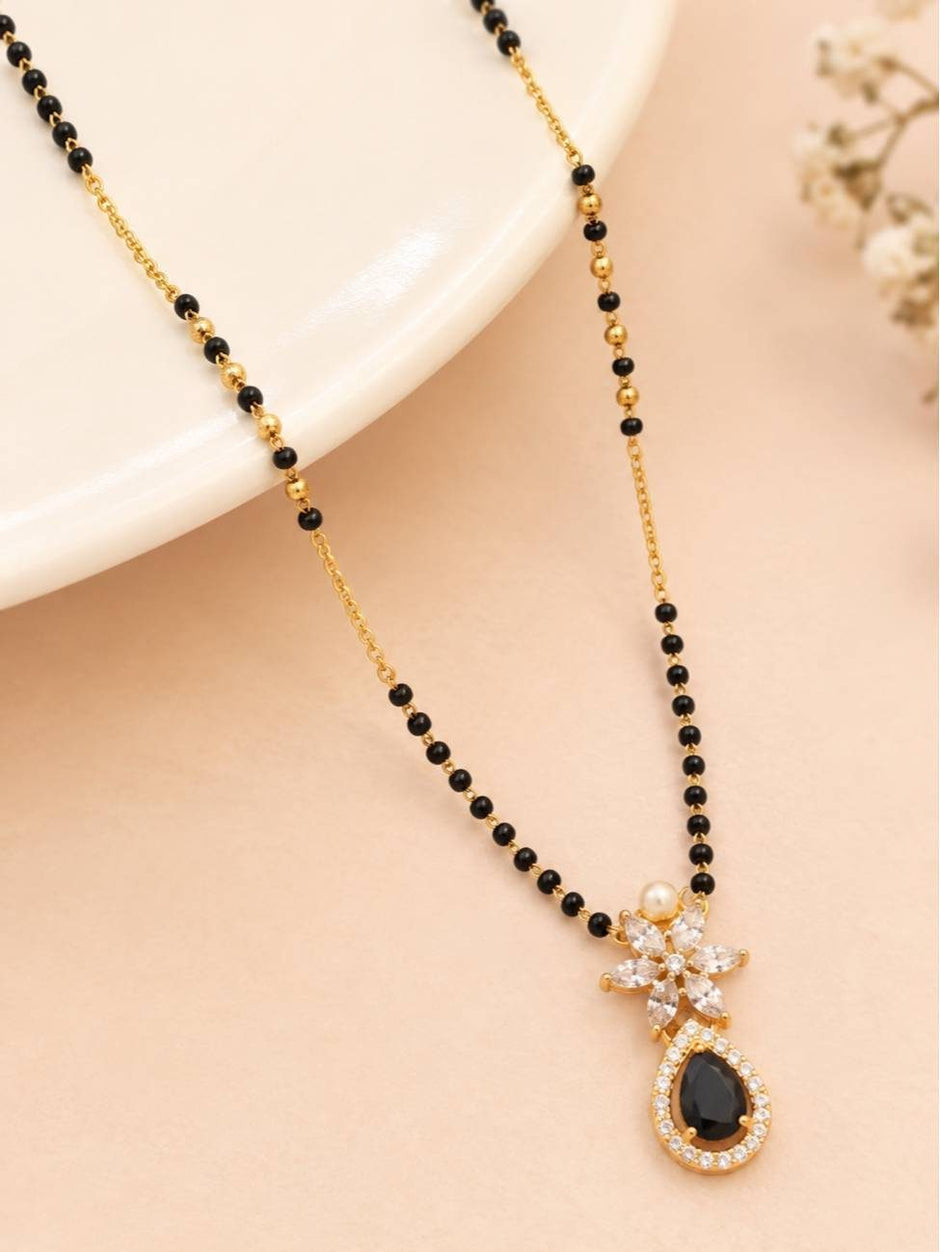 Black bead mangalsutra with white CZ marquise and black teardrop pendant on a cream stand with flowers