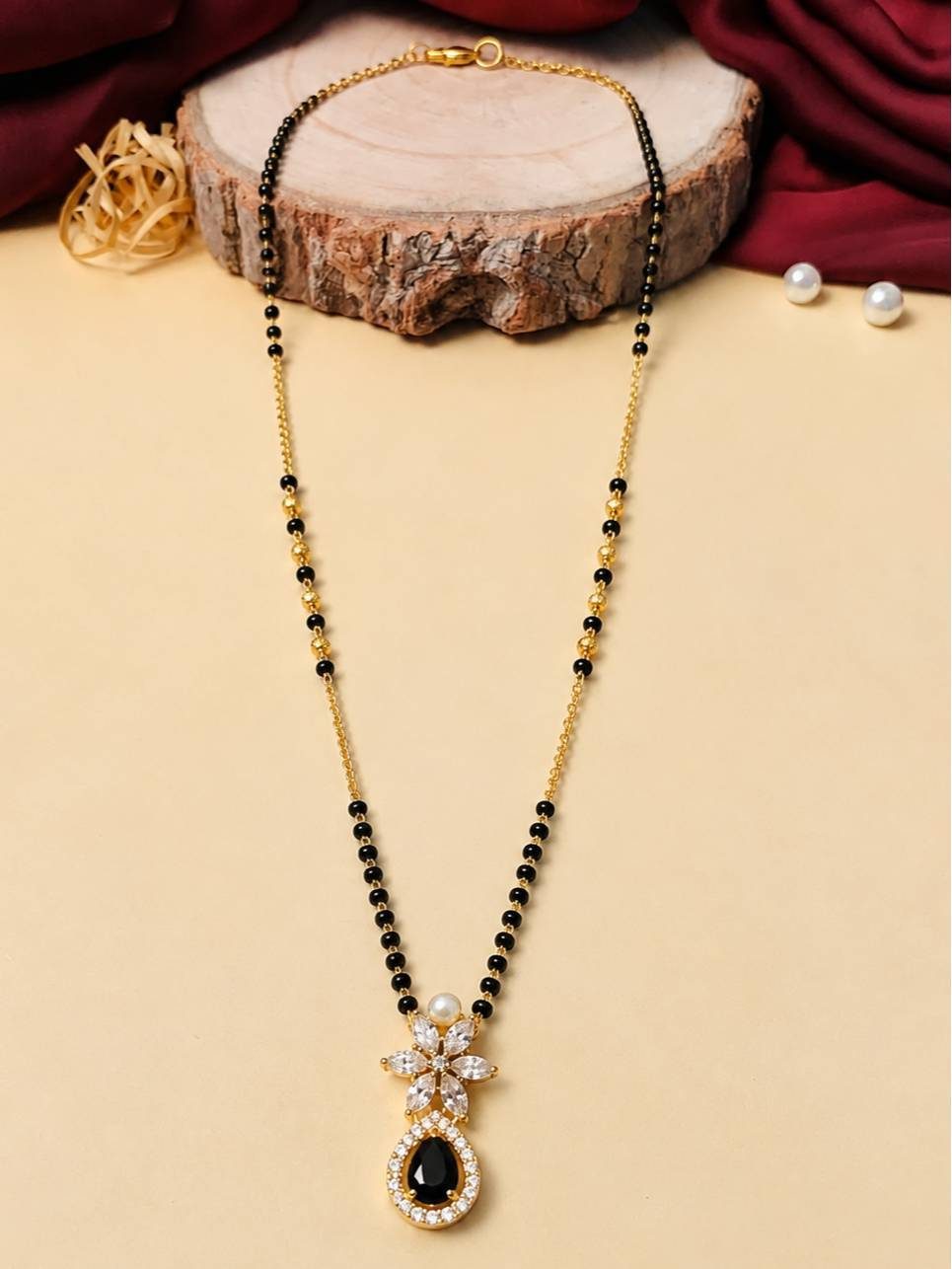 Full-length view of gold-plated black bead mangalsutra laid flat on a wooden slice against yellow background