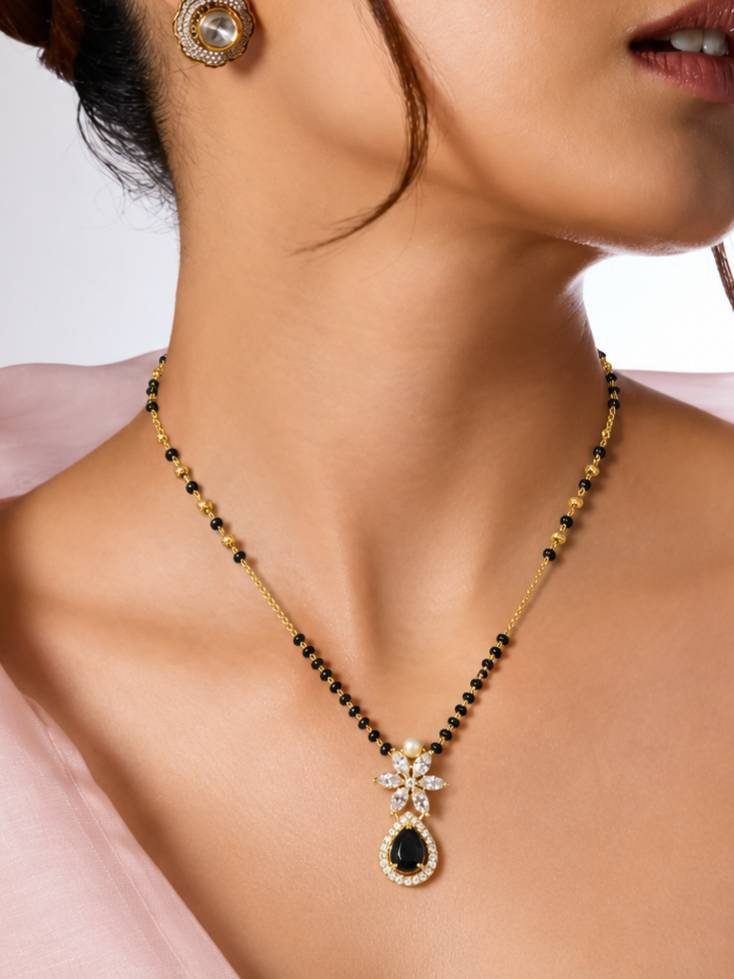Woman wearing gold-plated black bead CZ mangalsutra with matching floral stud earrings on bare neck