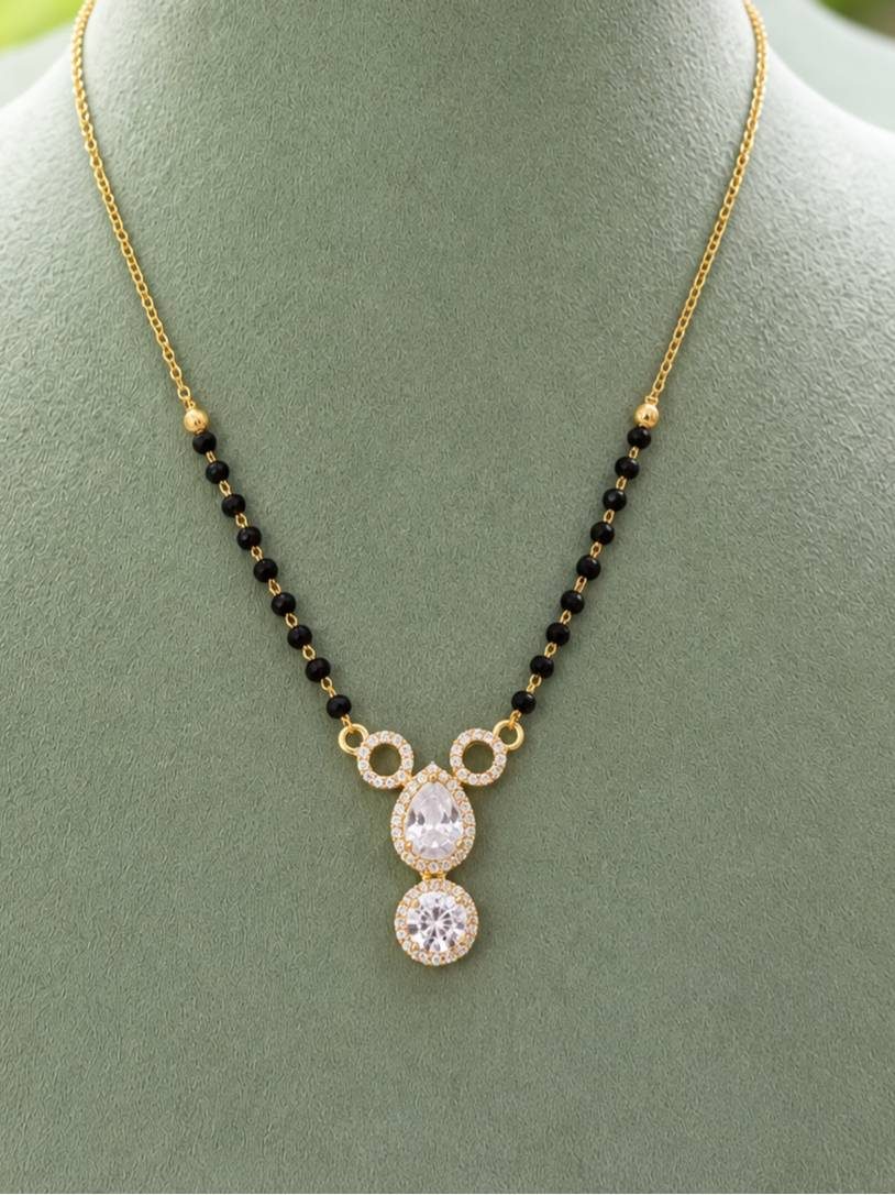 Gold-plated CZ mangalsutra with black beads and pear round halo pendant on green display bust