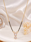 Gold-plated mangalsutra with cubic zirconia pendant laid flat on white satin with dried flowers