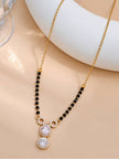 Close-up of gold-tone mangalsutra chain and CZ halo pendant on beige surface at an angle