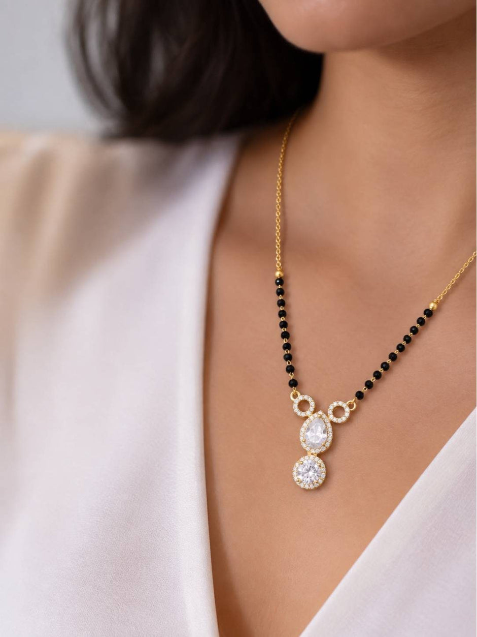 Model wearing gold-plated CZ mangalsutra with black bead strand over white v-neck top