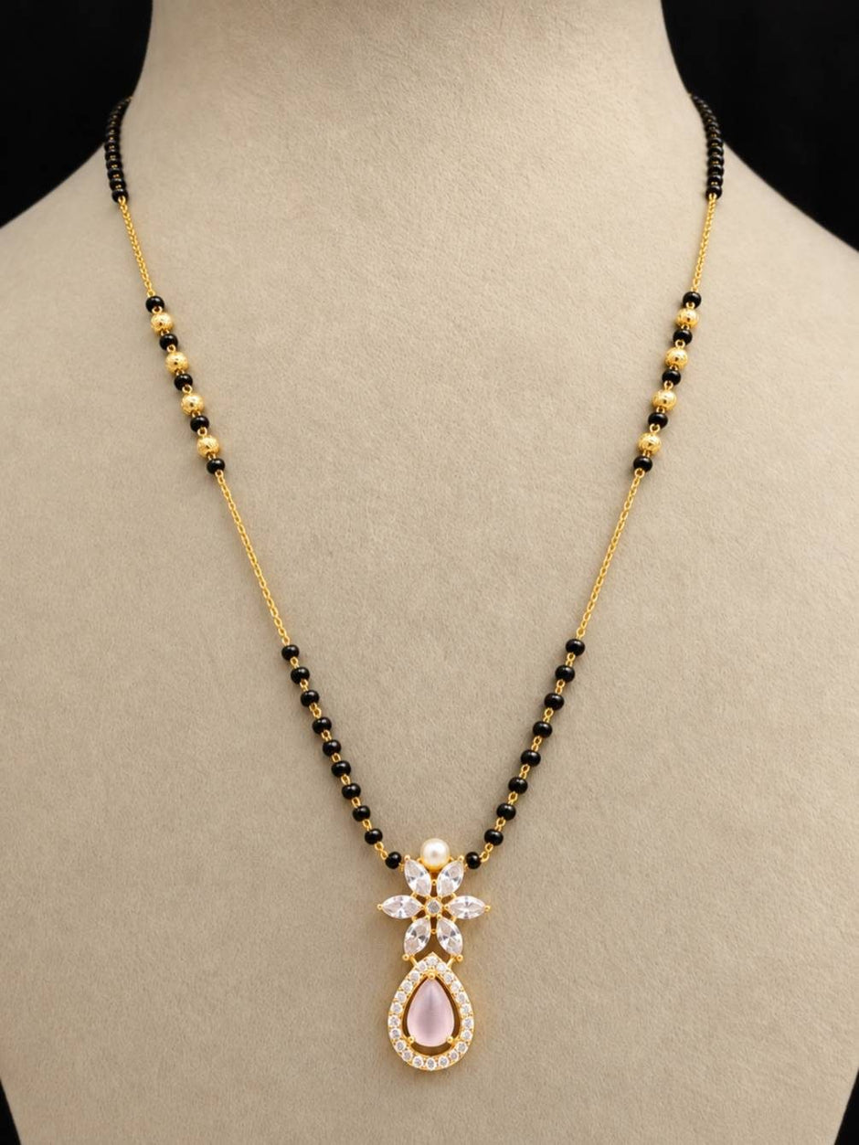 Gold-plated mangalsutra with black and gold beads displayed on a cream jewellery bust, showing CZ floral pendant with rose teardrop stone