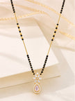 Gold-plated mangalsutra laid flat on a white surface with golden ribbon accent, highlighting the full length of the black bead chain and CZ pendant