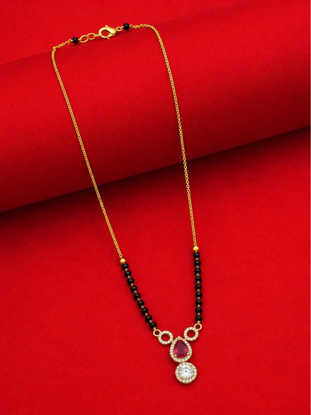 Full-length view of gold-plated black bead mangalsutra laid flat on red fabric showing lobster clasp and full chain length