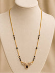 Gold-plated black bead mangalsutra displayed on a cream jewellery bust with CZ and red teardrop pendant
