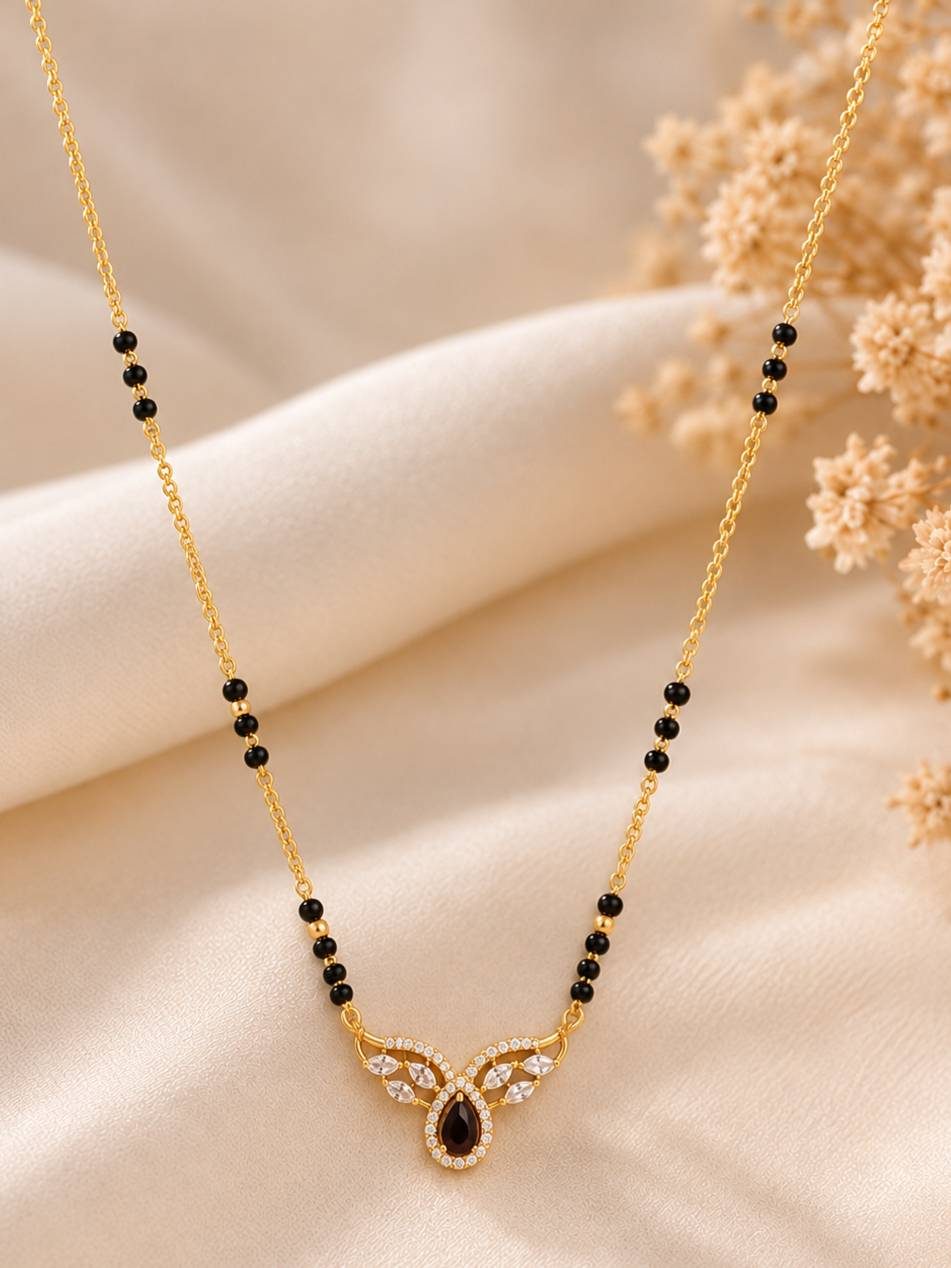 Close-up of gold-plated mangalsutra pendant with marquise CZ wings on ivory fabric with dried flowers