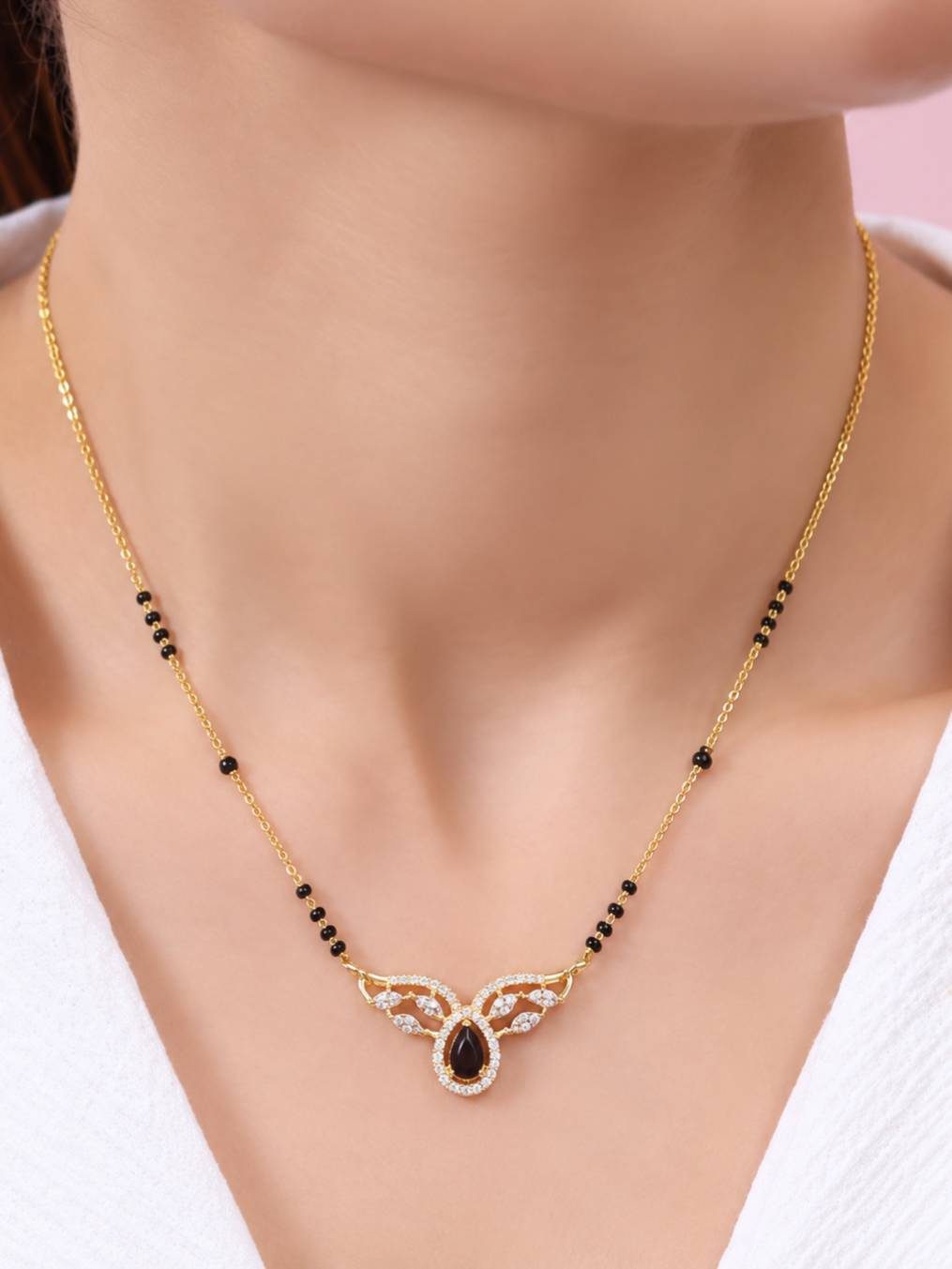 Gold-plated black bead mangalsutra worn around a woman's neck with white outfit showing full pendant detail