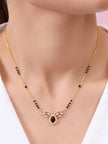 Gold-plated black bead mangalsutra worn around a woman's neck with white outfit showing full pendant detail
