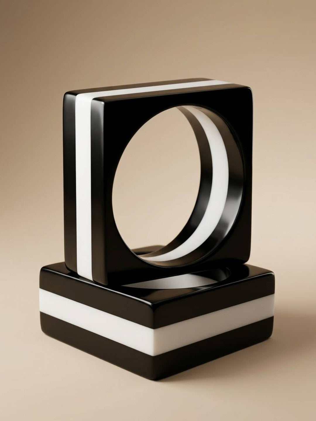 Two black and white striped resin square bangles stacked on a beige studio surface
