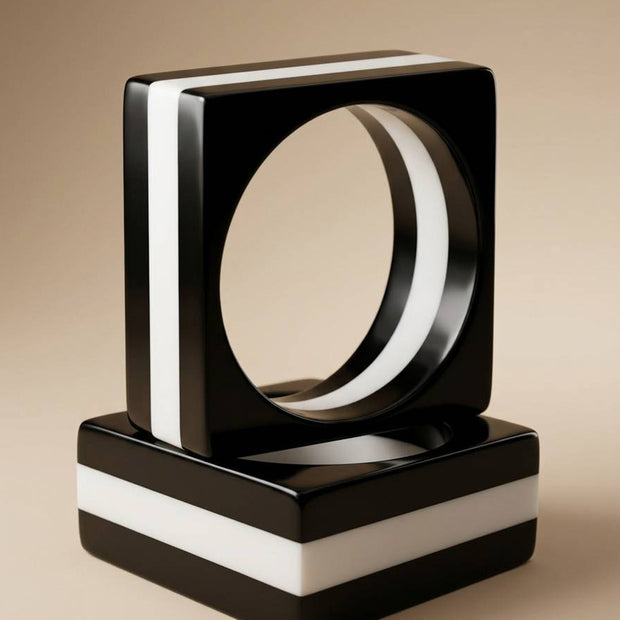 Two black and white striped resin square bangles stacked on a beige studio surface