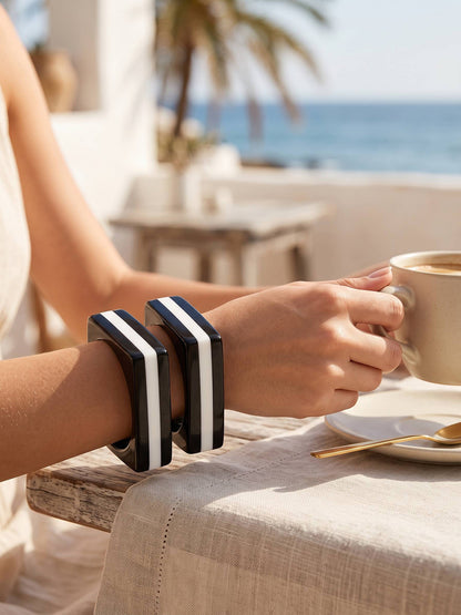 Woman wearing two black and white striped square resin bangles on wrist at a seaside cafe table